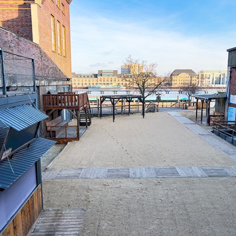 Blick von oben auf Außengelände mit Sandfläche vor Glashaus und Arena Club