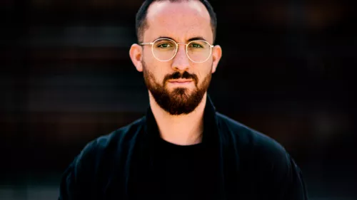 Igor Levit steht in schwarzem Hemd vor einem schwarzen Hintergrund.