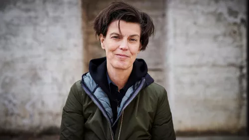 Carolin Emcke trägt eine grüne Jacke und kurze Haare. Sie steht vor einer Wand.