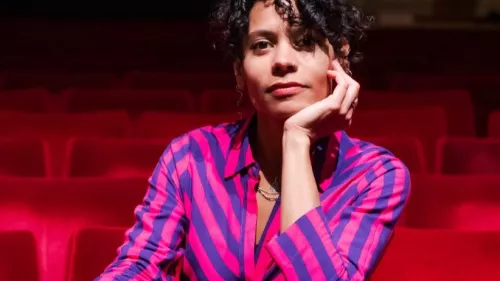 Auf dem Foto ist Emilia Roig in einem Theater- oder Kinosaal zwischen roten Vorstellungssesseln zu sehen. Sie trägt ein gestreiftes Oberteil und blickt direkt in die Kamera.