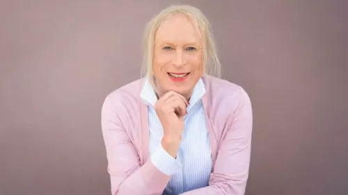 Georgine sitzt vor einem hellen Hintergrund. Sie trägt kinnlange Haare und lächelt in die Kamera.