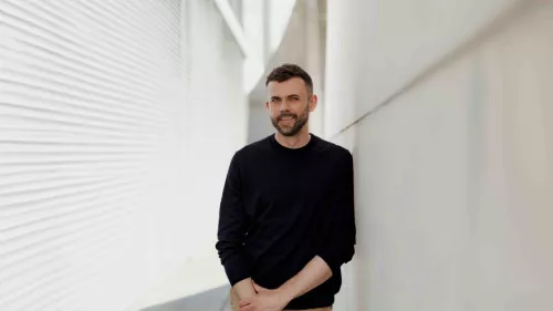 Ein Porträt von Janosch Delcker. Er trägt ein dunkles Sweatshirt trägt und lächelt in die Kamera, aufgenommen draußen in Berlin