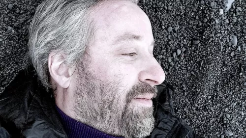 Portrait von Robin Berjon. Er liegt auf dem Boden und schaut nach rechts. Dabei trägt er eine Jacke, Rollkragenpullover sowie kurze Haare und Bart.