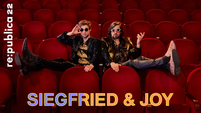 Die beiden Magier Siegfried und Joy sitzen in einer Stuhlreihe eines Theaters und legen die Beine über die vorderen Lehnen.