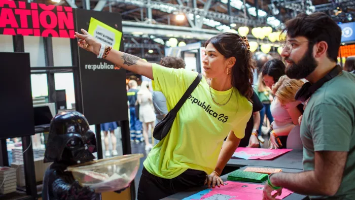 Volunteers auf der re:publica 23. Eine freiwillige Helferin weist einem Besuchenden den Weg.