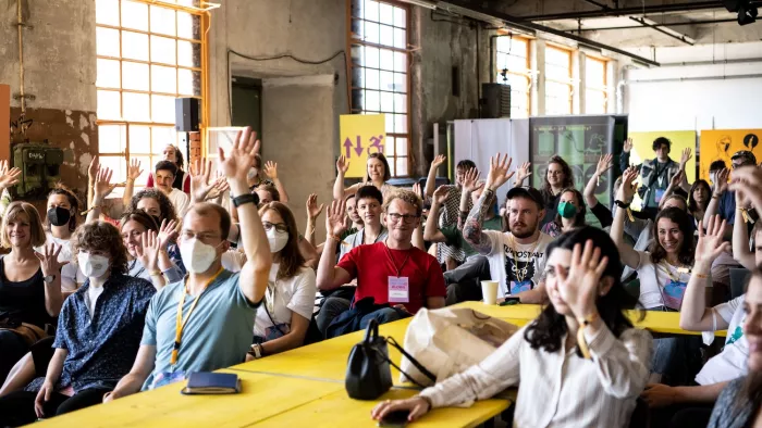Eine Workshop-Situation auf der re:publica. Viele Menschen sitzen an langen Tischen und heben die Hände.