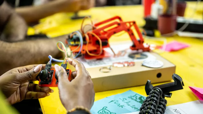 mehrere Hände werkeln im Makerspace – es sind Kabel und eine Plastikkonstruktion zu erkennen