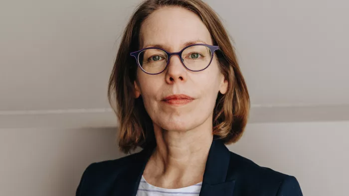 Anne Brorhilker hat einen Blazer und ein gestreiftes Oberteil an. Sie trägt Haare bis zu den Schultern und eine Brille. 