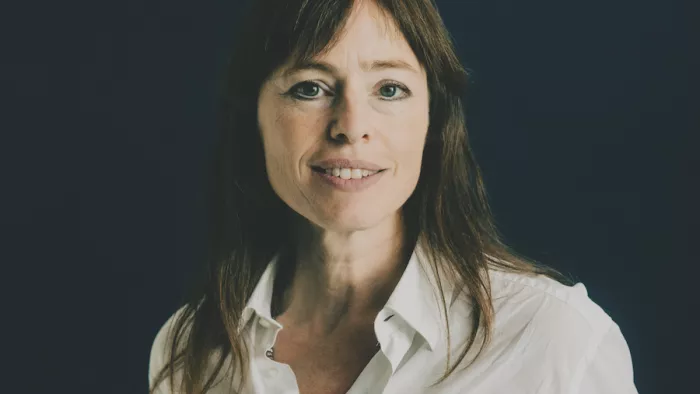 Hedwig Richter hat lange glatte Haare und trägt eine Bluse. Sie schaut in die Kamera und lächelt. Dabei steht sie vor einem dunklen Hintergrund.