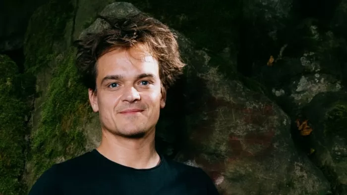 Foto von Patrick Stegemann. Er trägt ein dunkles Shirt und steht vor einem dunkelgrünen Hintergrund.