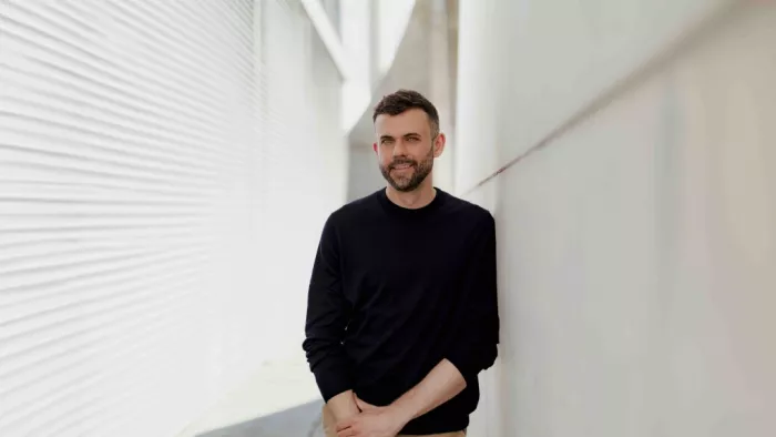 Ein Porträt von Janosch Delcker. Er trägt ein dunkles Sweatshirt trägt und lächelt in die Kamera, aufgenommen draußen in Berlin
