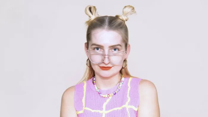 Foto von Isabelle Rogat. Sie trägt zwei Spacebuns, Lippenstift und eine Sonnebrille. Dazu ein Top mit Kette.