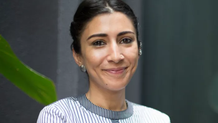 Foto von Urvashi Aneja. Sie lächelt in die Kamera trägt Bluse und Ohrringe.