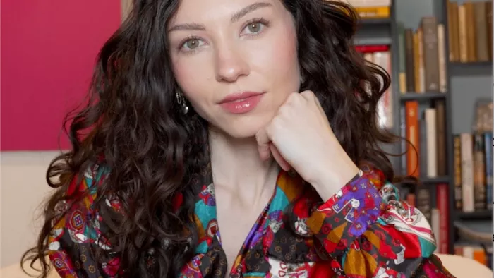 Foto von Jessica Burbank. Jessica trägt lange braune Haare und schaut in die Kamera. Sie sitzt auf einem Sofa in ihrem Wohnzimmer.
