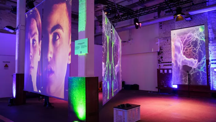 Foto einer Installation aus dem Off Stage Programm auf der republica. Zu sehen sind Screens mit Gesichtern und lilafarbenes und grünes Licht.