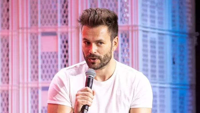 Tilo Jung auf der republica 23, er hält ein Mikrofon in der Hand und trägt ein weißes Shirt. Hinter ihm sind weiße Bäckerkisten als Bühnendeko zu erkennen.