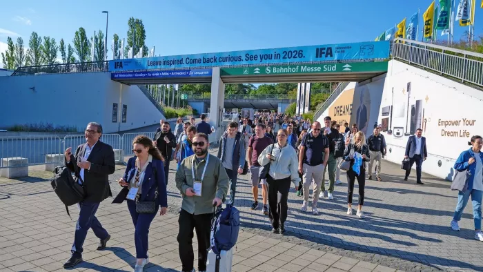 Einige Menschen laufen zur IFA. Sie haben teilweise Koffer dabei. Hinter ihnen befindet sich ein Banner mit Logo und Schriftzug der Internationalen Funk Ausstellung.