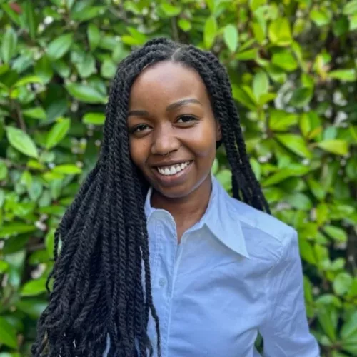 African woman with long dark hair, wearing a white shirt and smiling. Against a green background. 