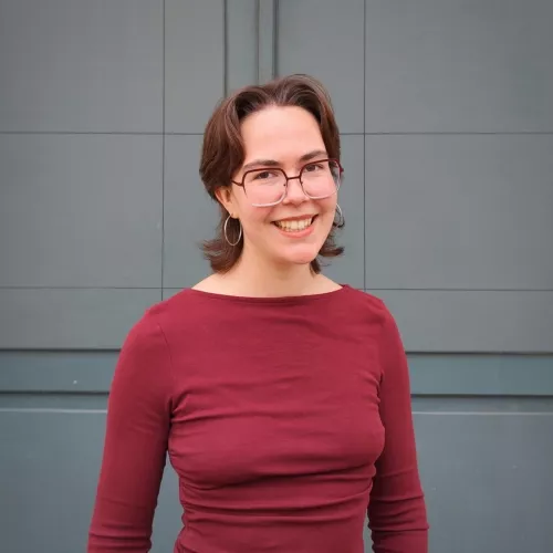 Leonie Heims steht vor einer grauen Fassade und blickt in die Kamera