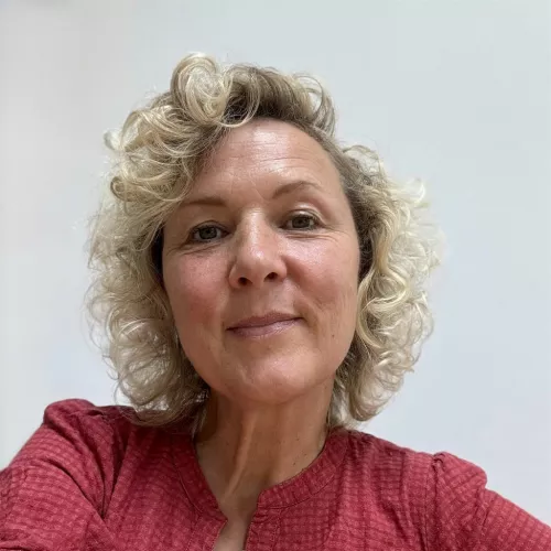Portrait von Ela mit weinrotem Hemd vor einem neutralen Hintergrund