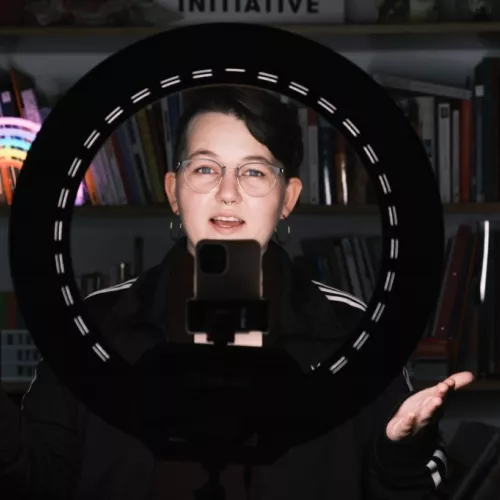 Eine Person steht hinter einem Ringlicht und spricht in eine Handykamera
