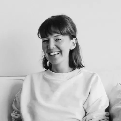 Black/White profile photo of Hanna sitting on a couch with a light sweater, dark hair, smiling into the camera