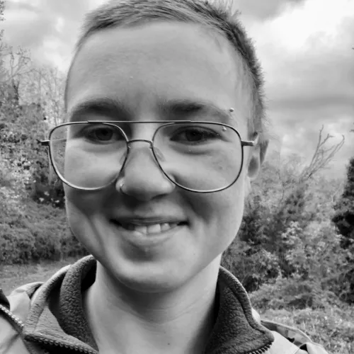 In schwarzweiß ist eine Person mit kurzen Haaren und einer Brille zu sehen. 