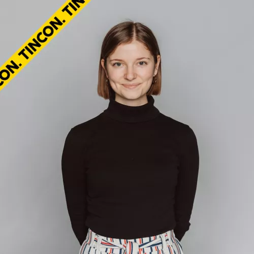 Auf dem Bild sieht man ein Portraitbild von Jule. Sie trägt einen schwarzen Rollkragenpullover und trägt ihre hellbraunen Haare als Bob. Sie lächelt in die Kamera.