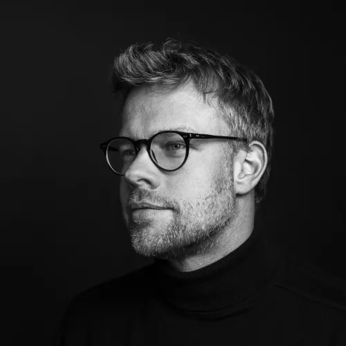 Mann mit drei Tage Bart und Brille im seitlichen Profil vor schwarzem Hintergrund