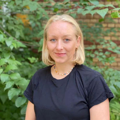 Foto von einer blonden Frau mit schwarzem T-Shirt vor grünem Strauch
