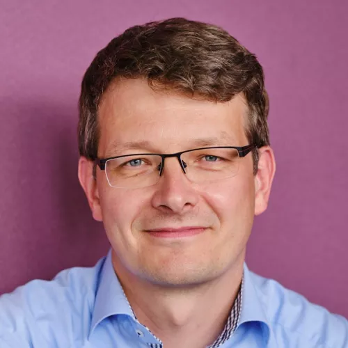 Profilfoto von Mario Wiedemann vor einem fliederfarbenen Hintergrund.