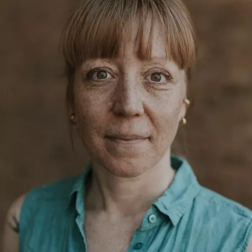 Portraitbild: Frau mit rötlichem Haar, Sommersprossen und Dutt in grüner Bluse 