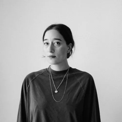 Portrait of a woman with dark shirt in front of white wall. 