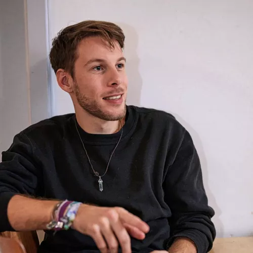 beginning 30s, white male, short brown hair, black sweater, sitting and pointing