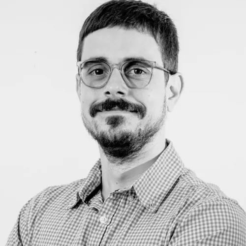 Profile image of André Ramiro in black and white: very short hair, glasses, a mustache, and a short beard.