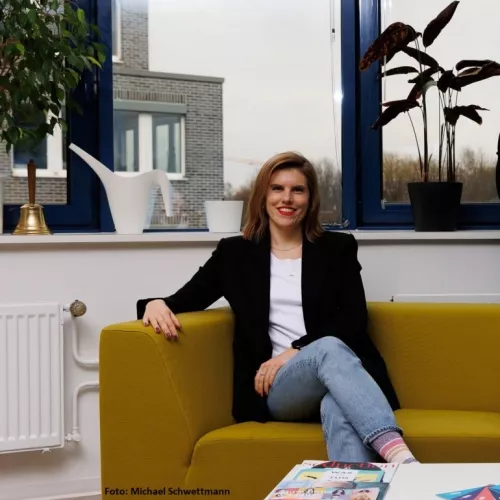 Weibliche Person die auf einem gelben Sofa sitzt und in die Kamera lächelt 