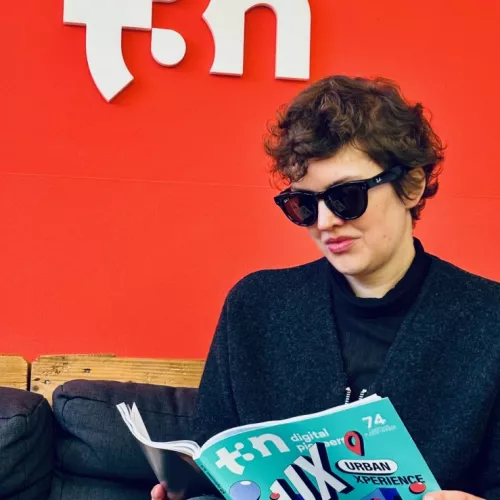 T3n-Chefredakteurin Sabrina Schadwinkel sitzt mit einer Magazinausgabe in der Hand vor einer roten Wand, die das t3n-Logo zeigt.