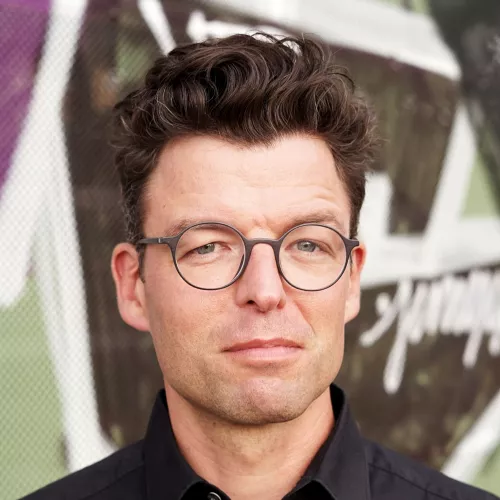 Ein Gesicht mit Brille vor einer bunten Wand