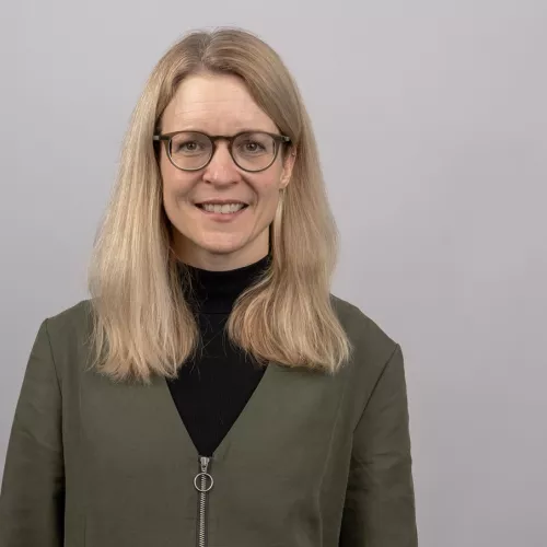 dunkelblonde lange Haare, runde hellbraune Brille, lächelnd