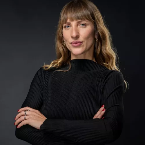 Porträt von Lisa Jikeli vor dunklem Hintergrund, mit verschränkten Armen und schwarzem Oberteil.