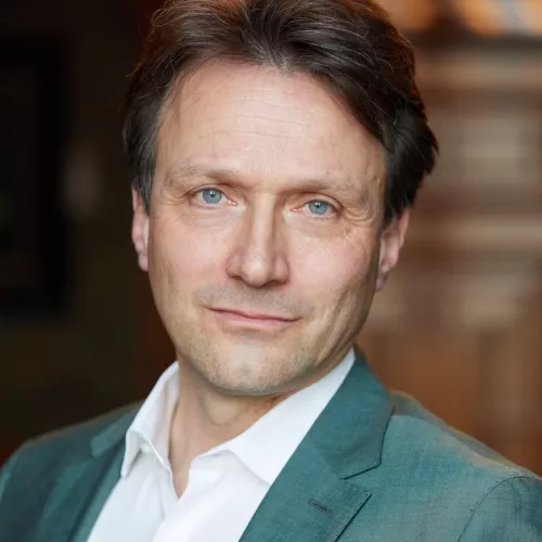 Wolfgang Blau trägt ein weißes Hemd und einen grünes Jacket