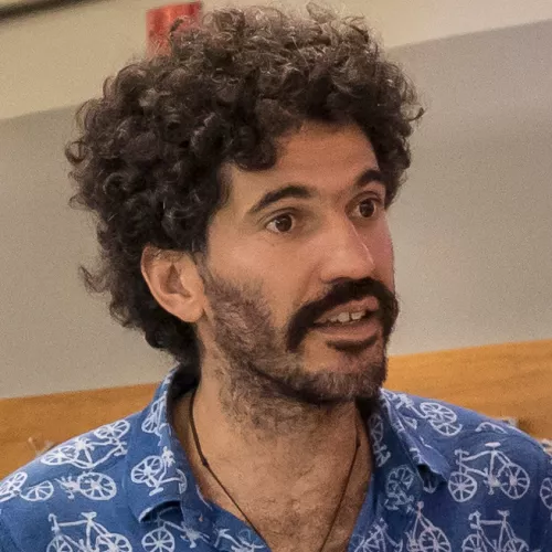 Photo of a man with curly hair, tan skin, and a blue t-shirt with bicycle details.