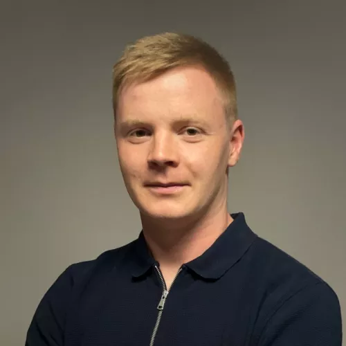 Profilbild von Fabian Reinold: Mann in dunkelblauem Polo-Hemd vor grauer Wand