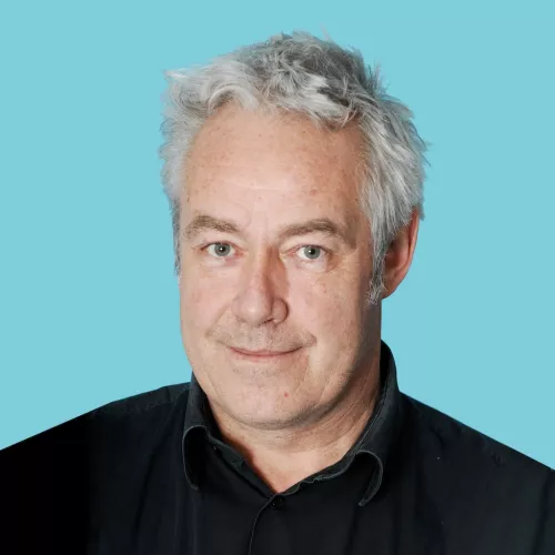 Michael trägt ein dunkles Hemd und steht vor einem blauen Hintergrund.