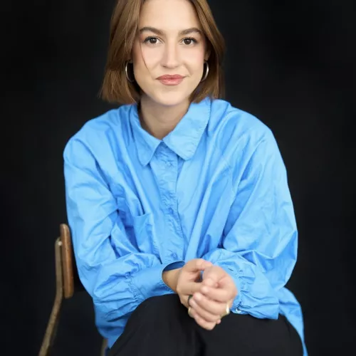 Victoria Reichelt sitzt in einem blauem Hemd auf einem Stuhl und lächelt in die Kamera  
