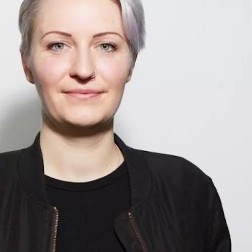 Profile picture of Kathy Meßmer, with short white hair and dressed in black.